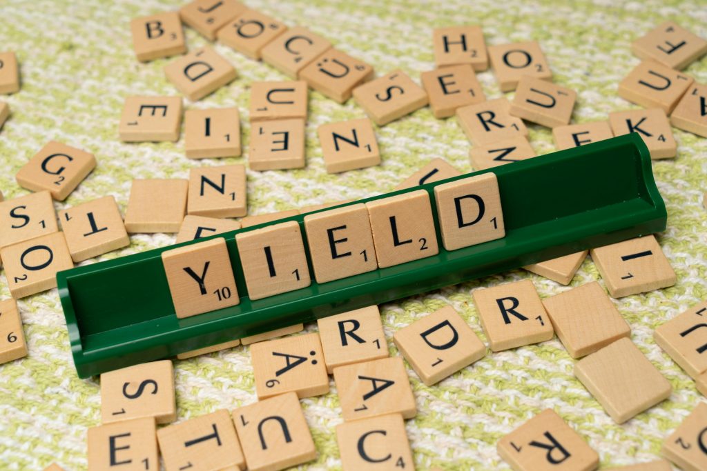 Scrabble tiles spelling 'Yield' on a rack among scattered letters.