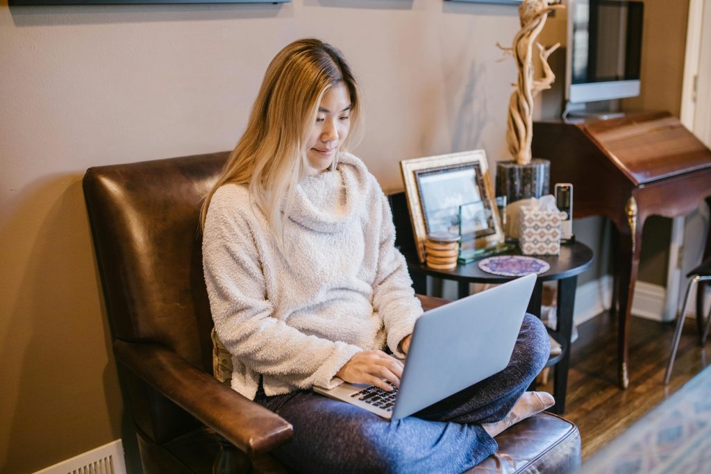 Woman seated on a chair using a laptop, enjoying a cozy home office environment.